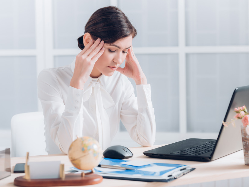 A photo of a woman having a headache while at work.